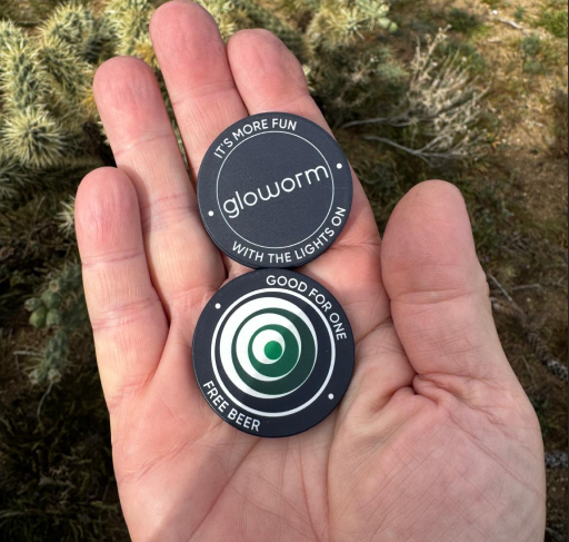 Gloworm-branded poker chip giveaway token held in hand at the 24 Hours at Old Pueblo 2026.